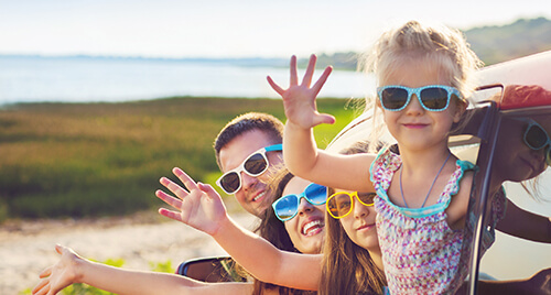 Car Insurance: Young family with two little girls waving out the car windows